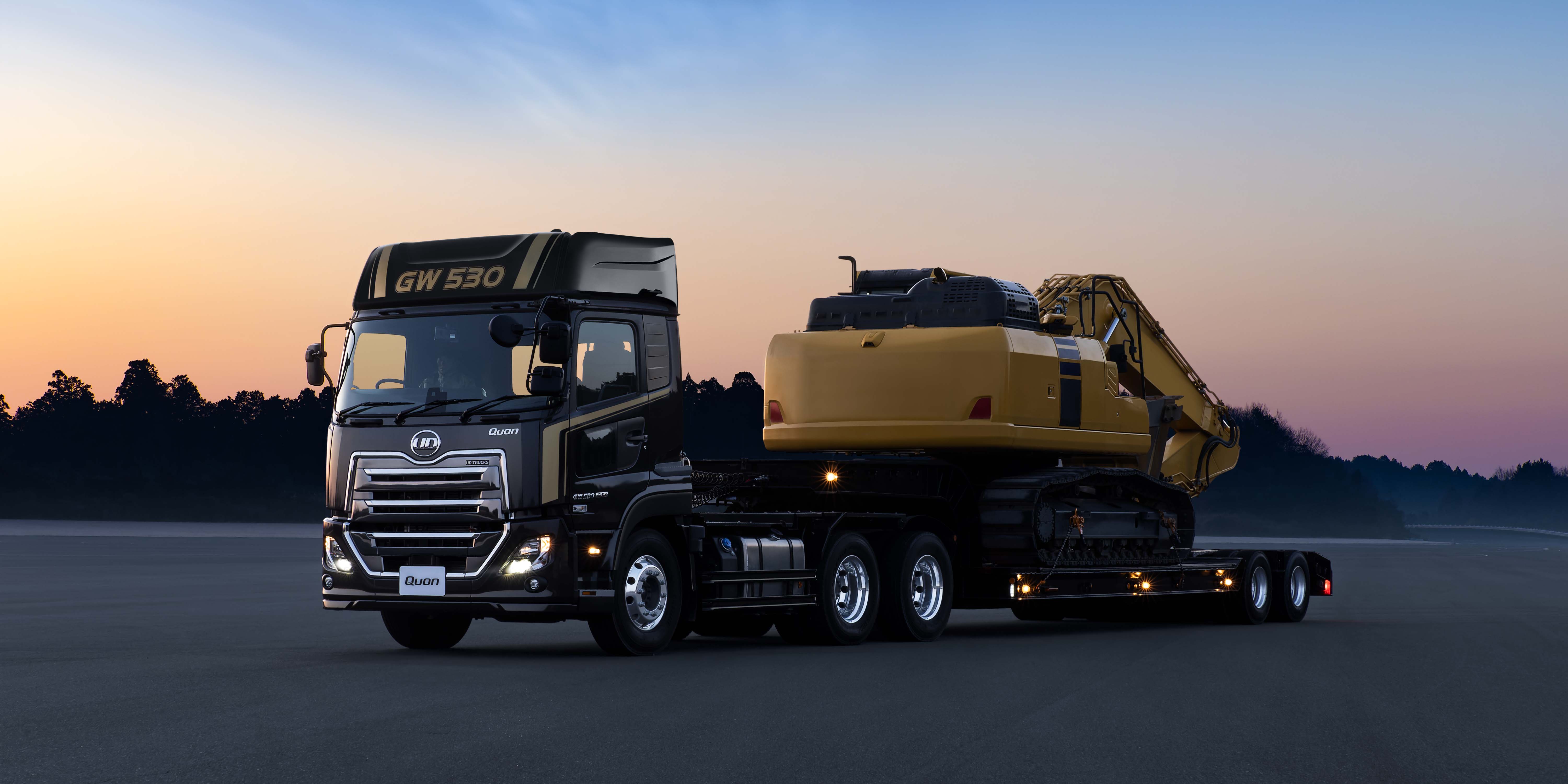 大型ダンプトラックがショベルカーを積んで夕暮れの道路を走行