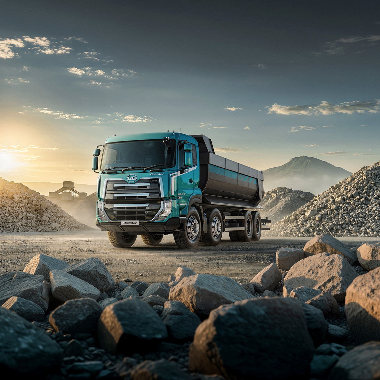 Blue dump truck on a gravel lot at sunrise with mountains in the background.