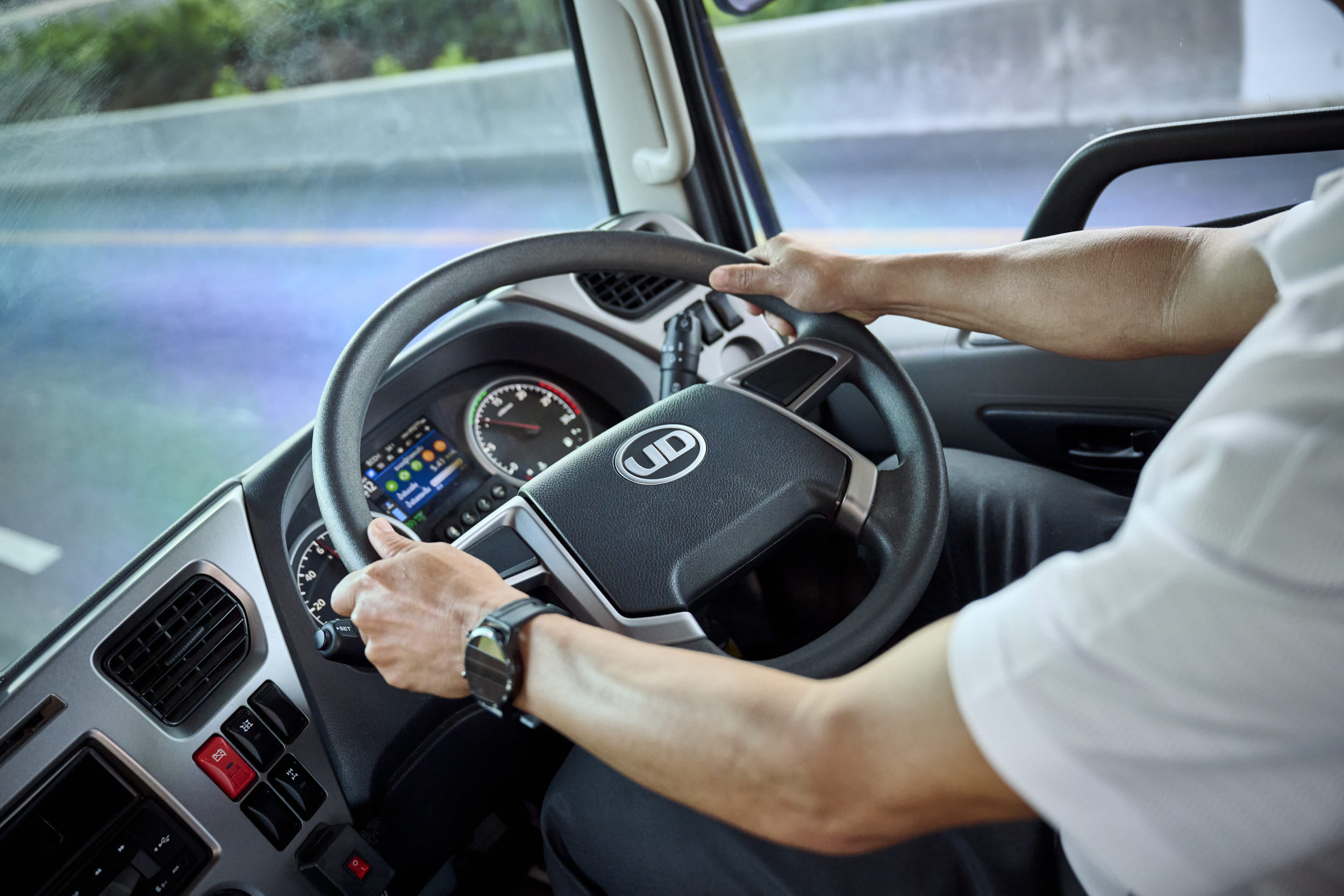 Person driving a commercial truck, hands on the steering wheel, dashboard visible.