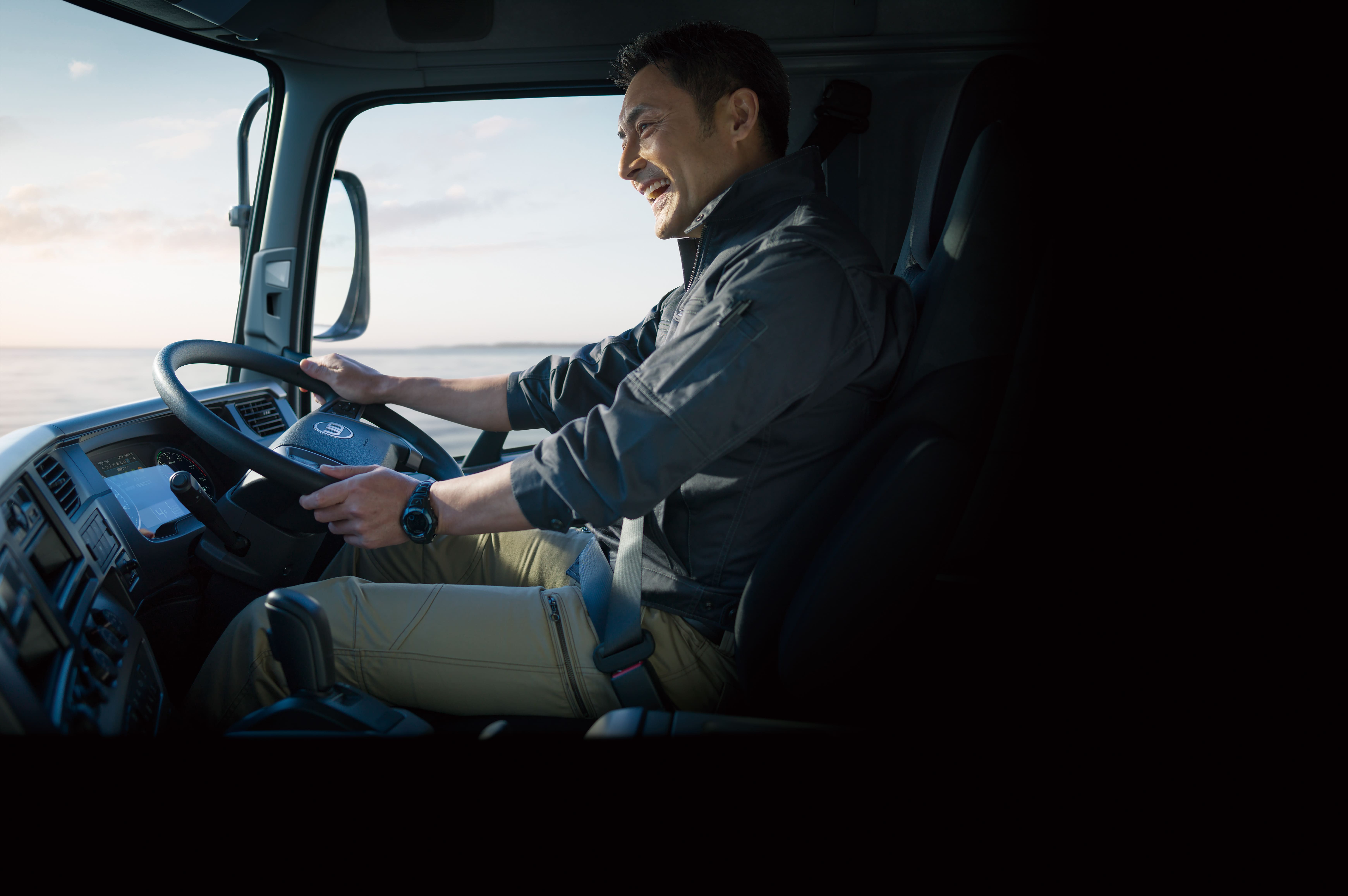 Man smiling while driving a truck in daylight.