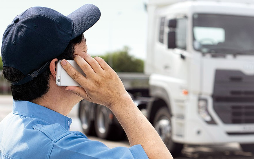 Person in uniform talking on phone near a white truck on a road.