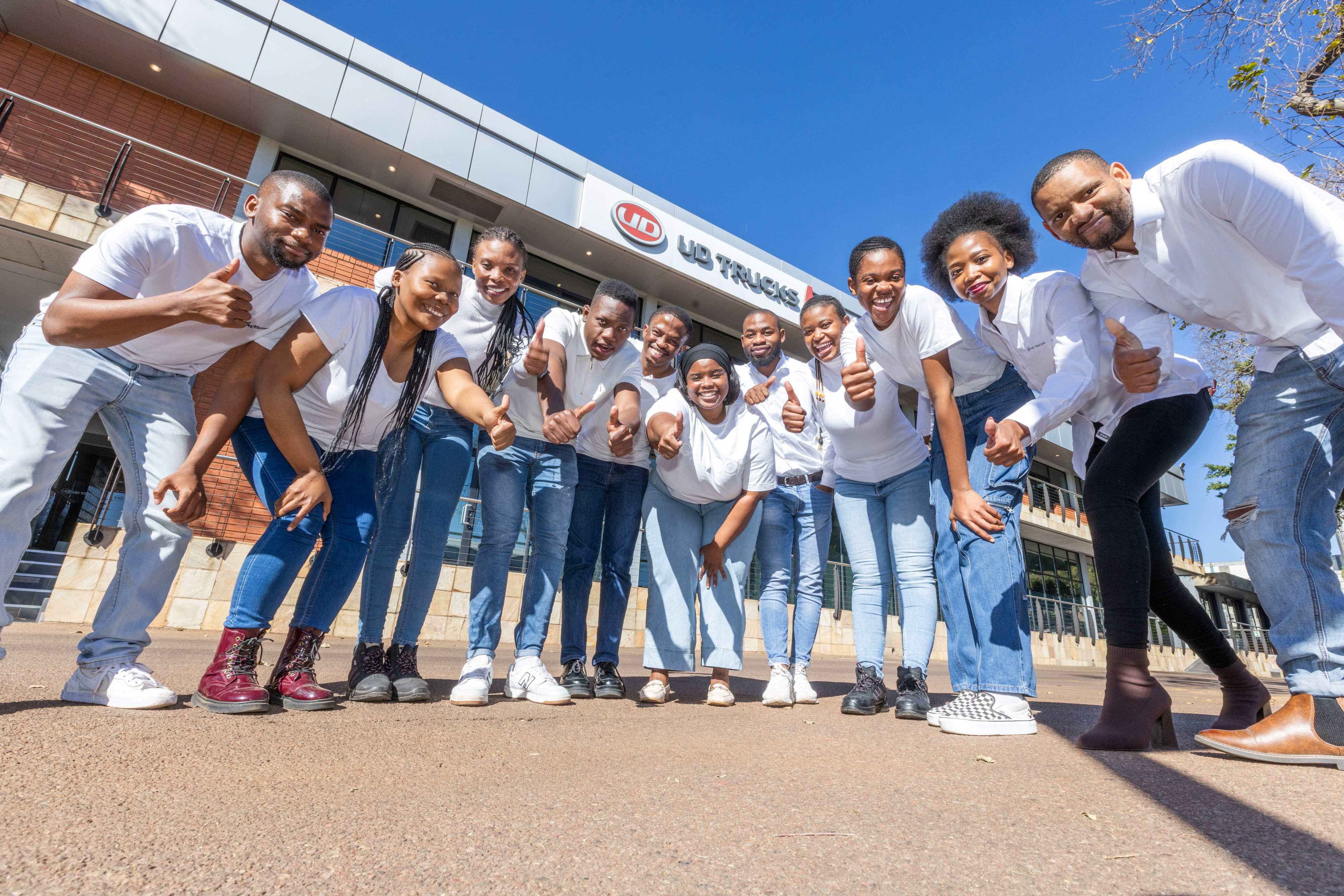 Groep glimlaggende mense in wit hemde buite op 'n sonnige dag.