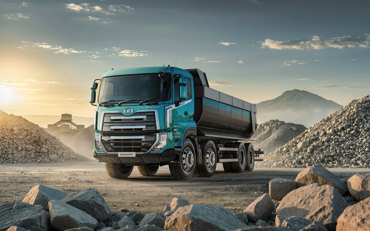 Blue dump truck on a gravel site at sunrise, surrounded by rocks and mountains.