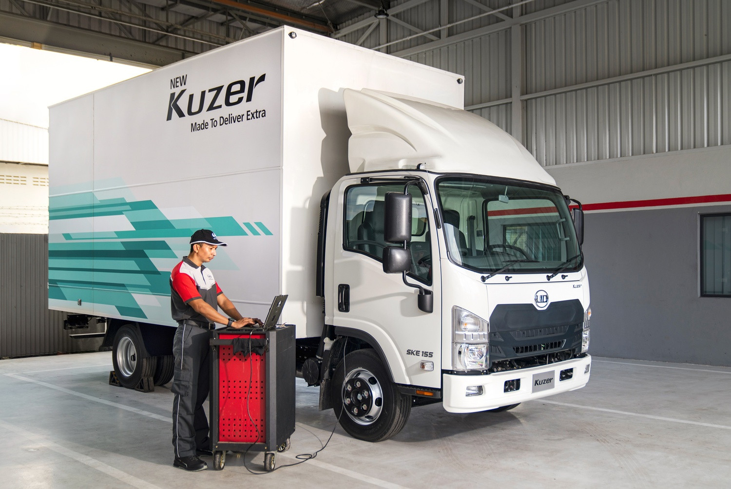Mechanic using diagnostic equipment next to a white Kuzer delivery truck in a garage.