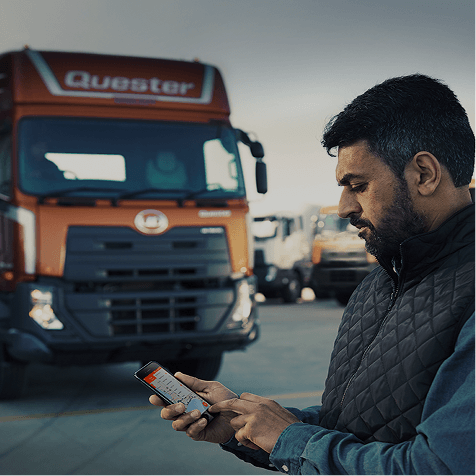 Hombre usando celular frente a un camión rojo en un estacionamiento.