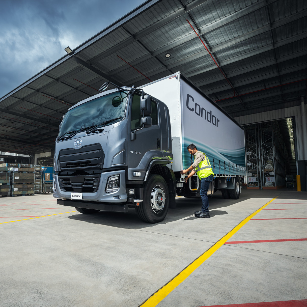 Gray delivery truck parked at a warehouse while a worker inspects it.