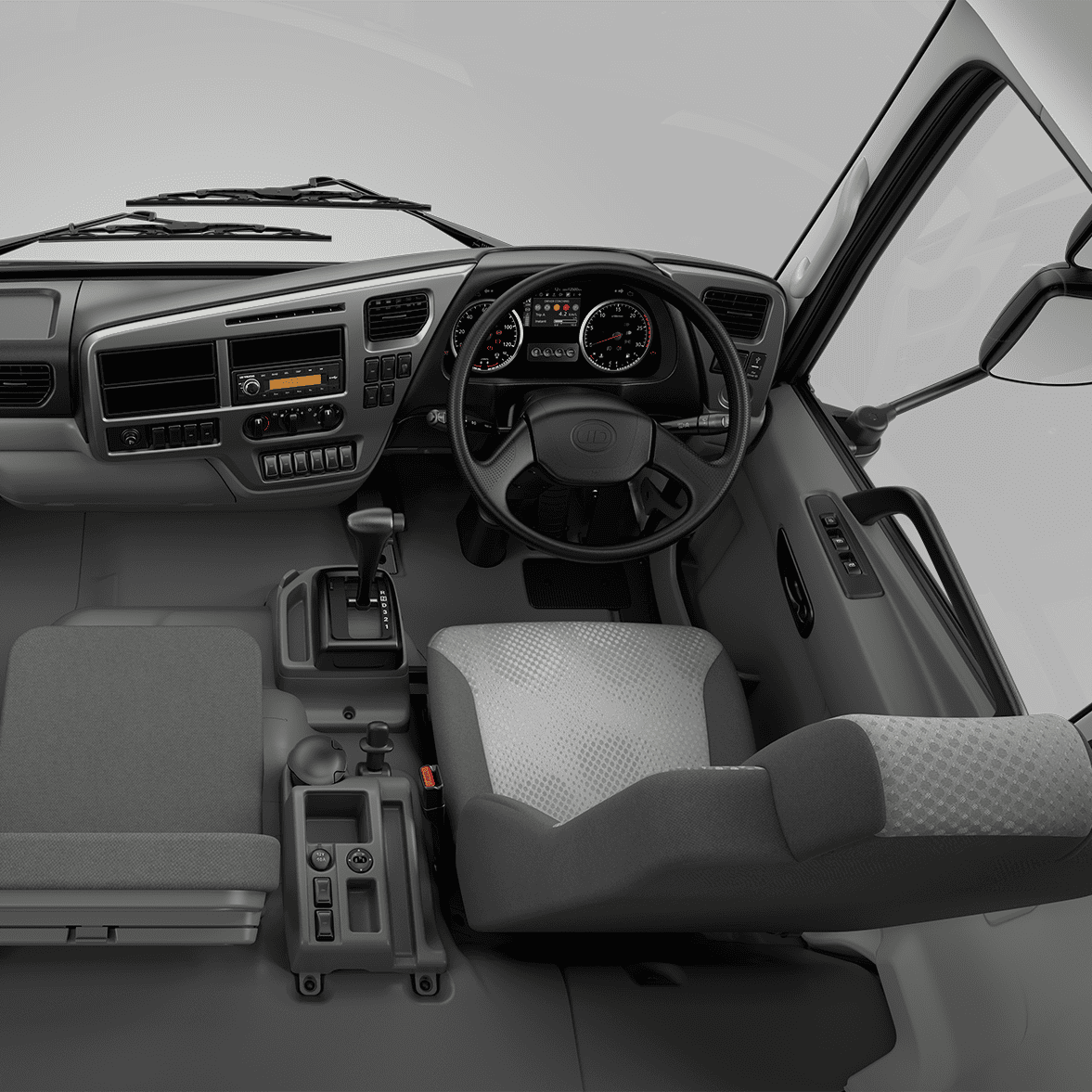 Stuurwiel en dashboard van 'n vragmotorkajuit, grys sitplekke, moderne instrumente.