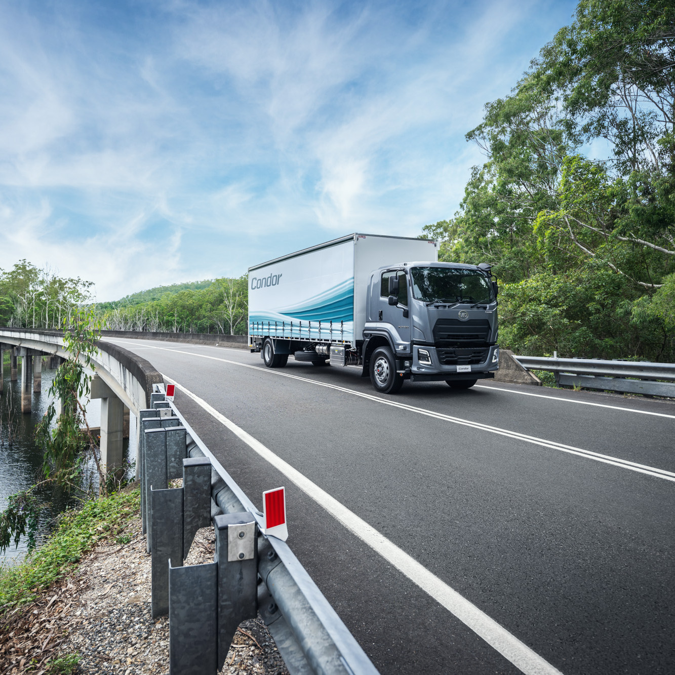 Truck driving on a curved road beside trees under a blue sky