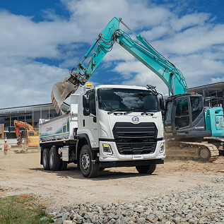 Excavator loading dirt into a white dump truck at a construction site under blue sky.