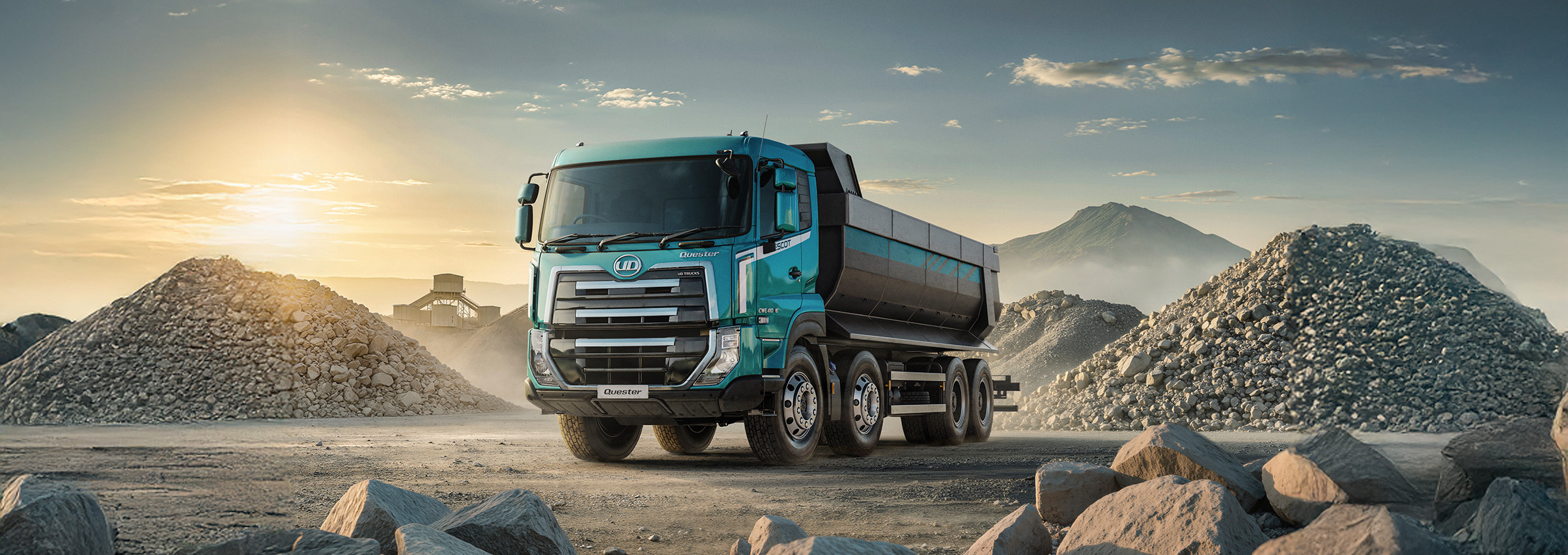 Blue dump truck on a rocky construction site at sunrise, with gravel piles in the background.