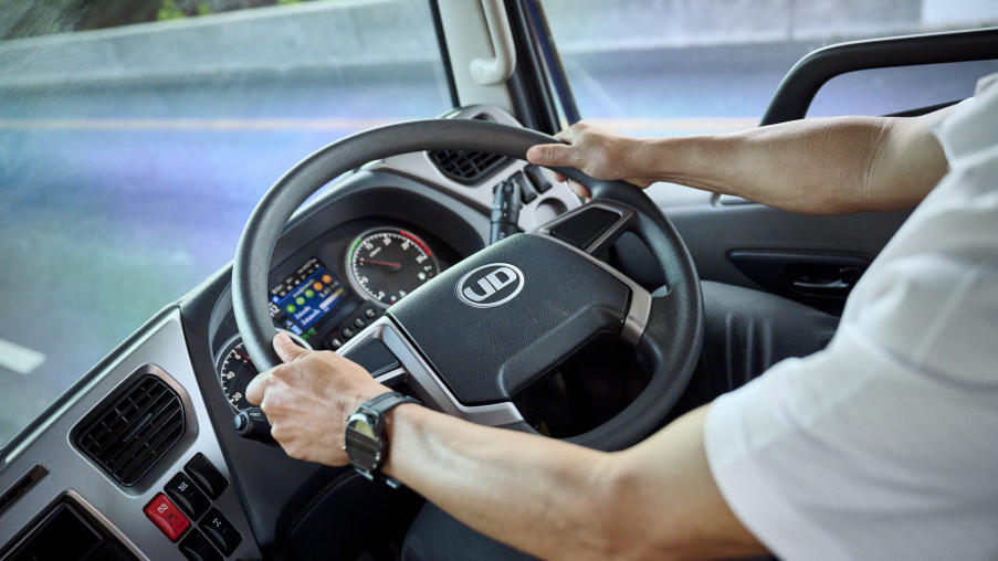 Person driving a commercial truck, hands on the steering wheel, dashboard visible.