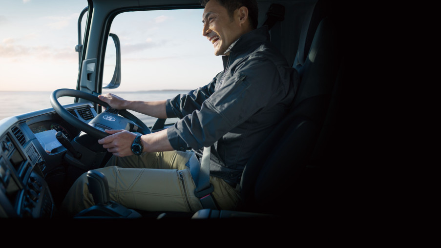 Man smiling while driving a truck in daylight.