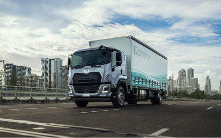 Large truck driving on city road with tall buildings in the background.