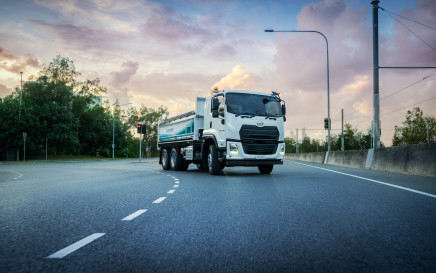 Large white truck driving on an empty road at sunset.