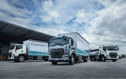 Three Condor delivery trucks parked outside a warehouse on a cloudy day.