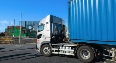 Truck hauling a blue shipping container at a freight yard under a clear sky.
