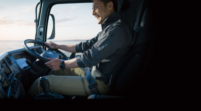 Man smiling while driving a truck in daylight.