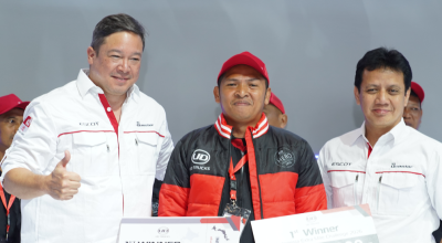 Tiga pria berpose bersama, satu mengenakan jaket hitam dan topi merah.