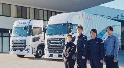 白い大型トラックの前で笑顔の作業着のスタッフ4人が並んでいる