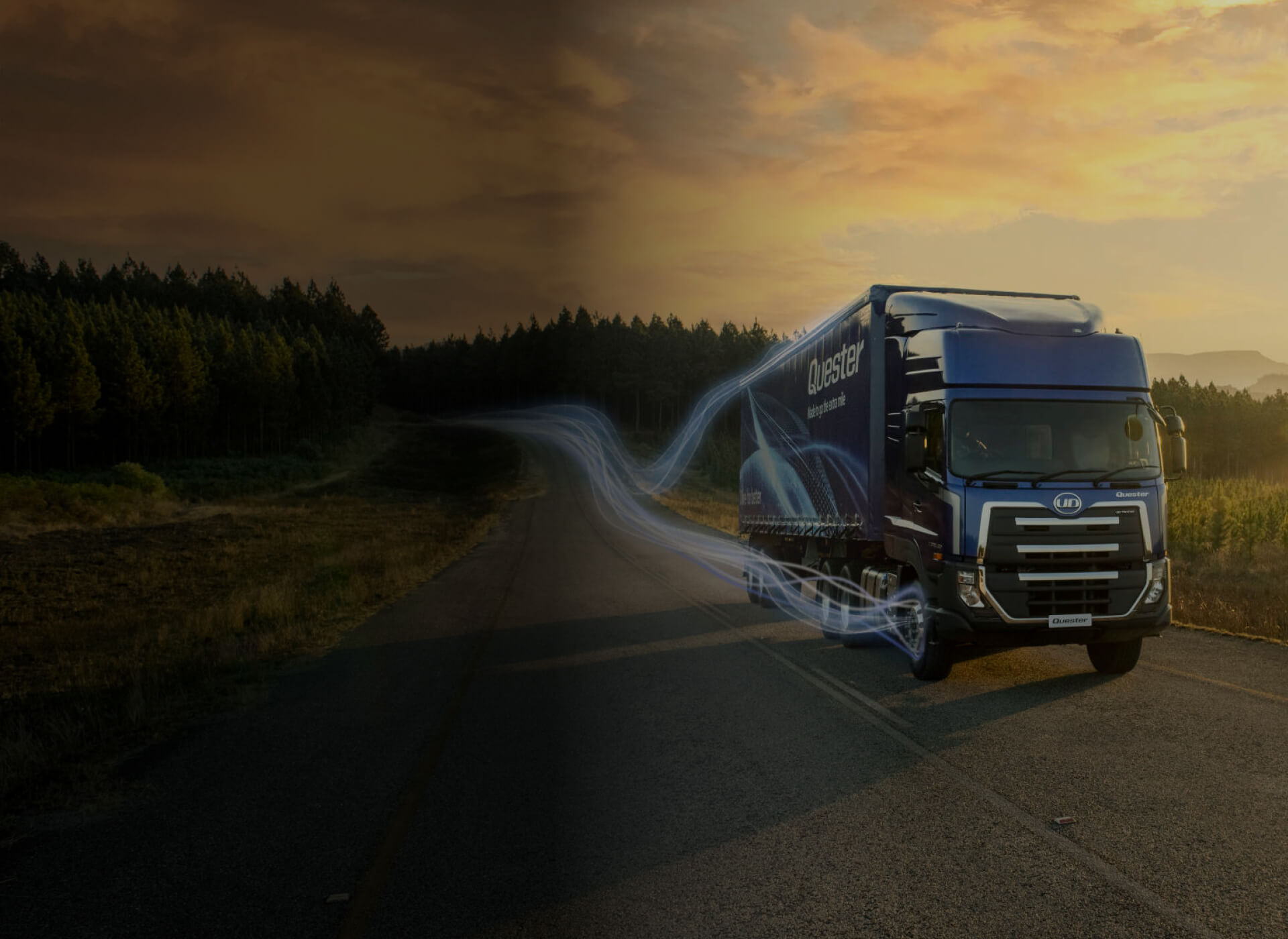 Truk biru besar melaju di jalan raya saat matahari terbenam.