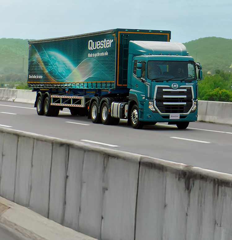 Tráiler azul con remolque en carretera, montañas verdes al fondo.