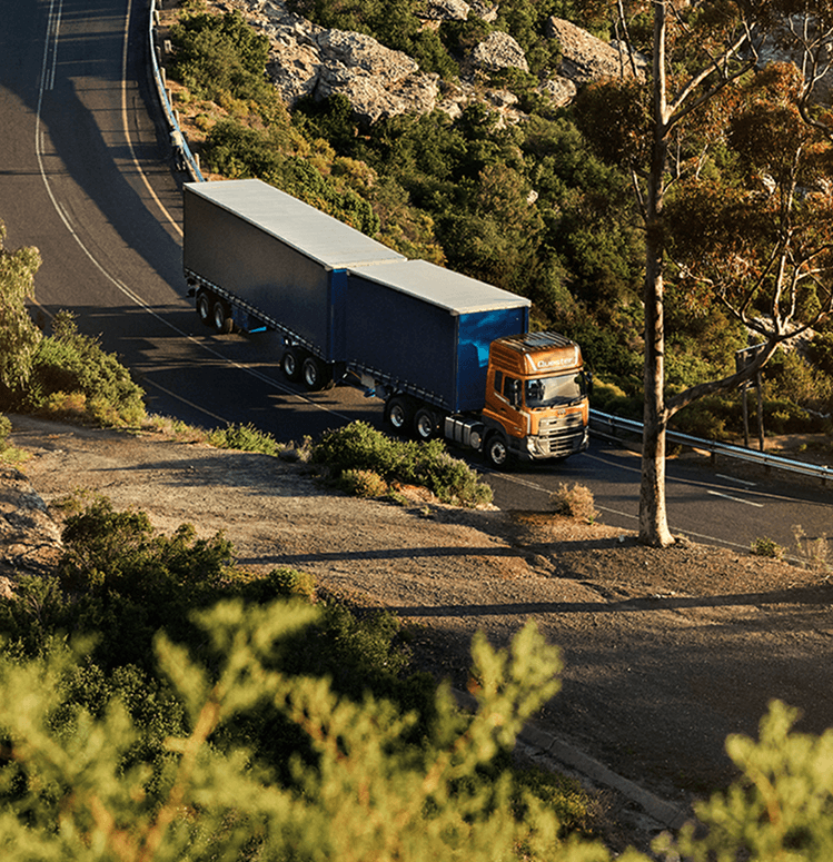 Truk besar melaju di jalan berkelok di tengah pepohonan dan semak.