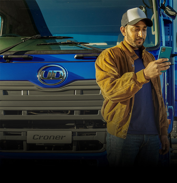 Man in a brown jacket using a smartphone in front of a blue truck.