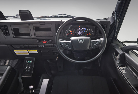 Truck cabin dashboard with steering wheel, control buttons and black seats.