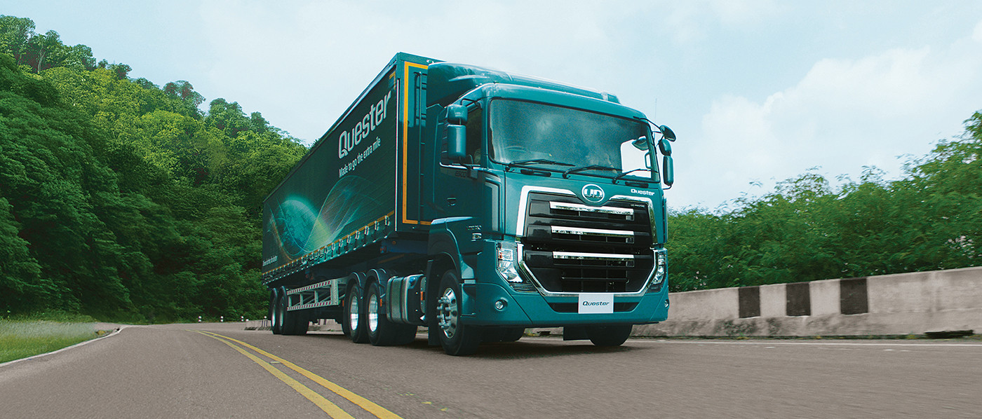 Blou vragmotor ry op 'n stil, geboë pad met bome aan die kant.