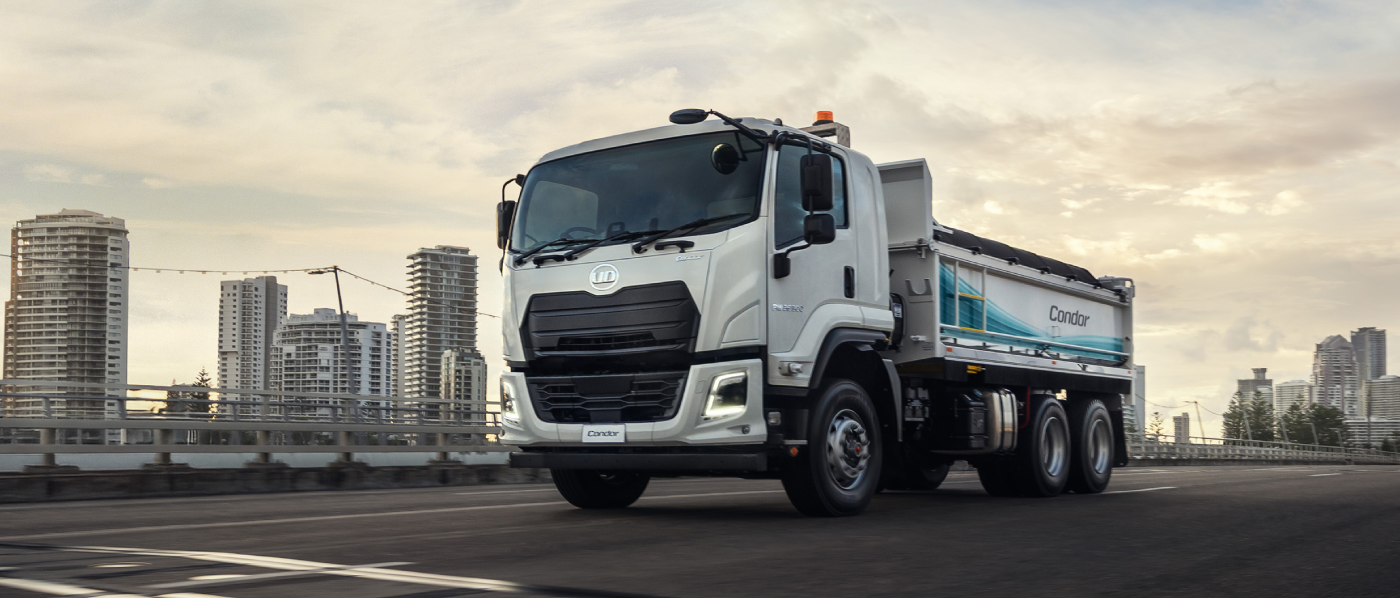 White dump truck on city street with high-rise buildings in the background at dusk.